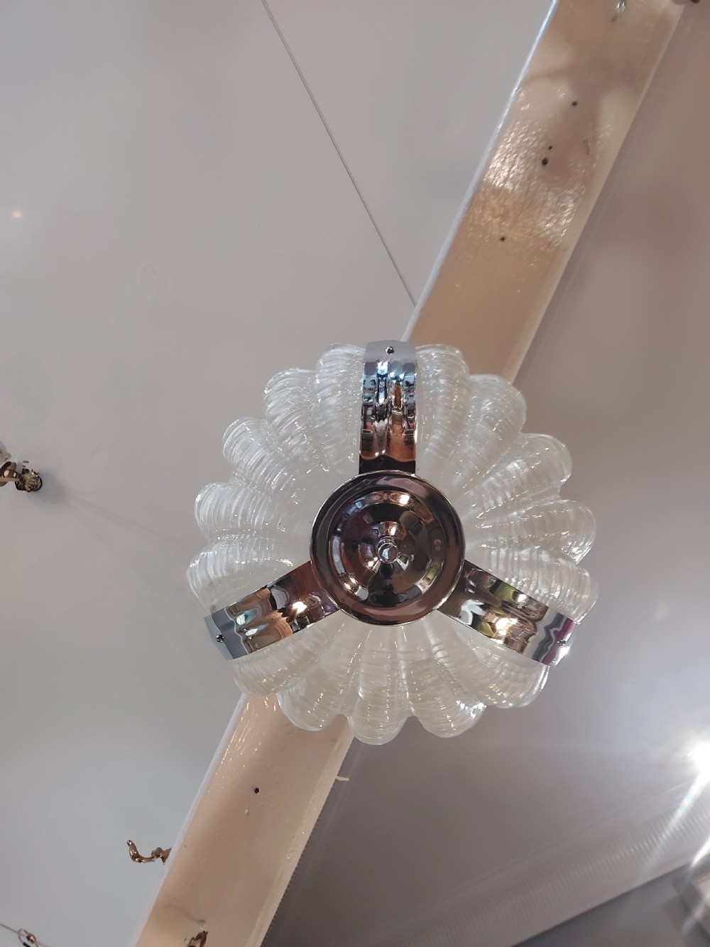 An Art Deco ceiling light fixture featuring three cream frosted glass clam shell shades held together by chrome brackets and suspended by three metal chains. View V
