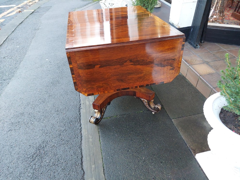 A Regency rosewood drop-leaf sofa table with twin inlaid drawers, a carved parcel gilt pedestal column, and a quadruped base ending in scroll feet. View V