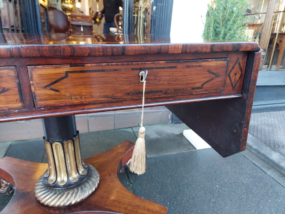 A Regency rosewood drop-leaf sofa table with twin inlaid drawers, a carved parcel gilt pedestal column, and a quadruped base ending in scroll feet. View VI