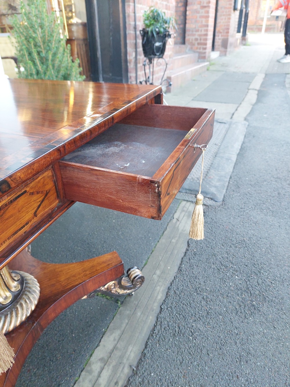 A Regency rosewood drop-leaf sofa table with twin inlaid drawers, a carved parcel gilt pedestal column, and a quadruped base ending in scroll feet. View IX