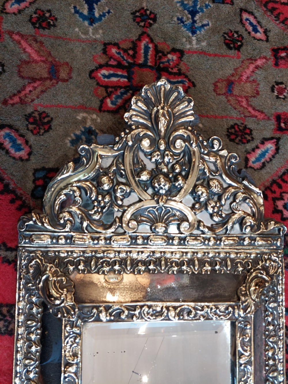 An early nineteenth-century Dutch style wall mirror featuring embossed repousse brass metalwork and a decorated crest over a central glass plate. View IV