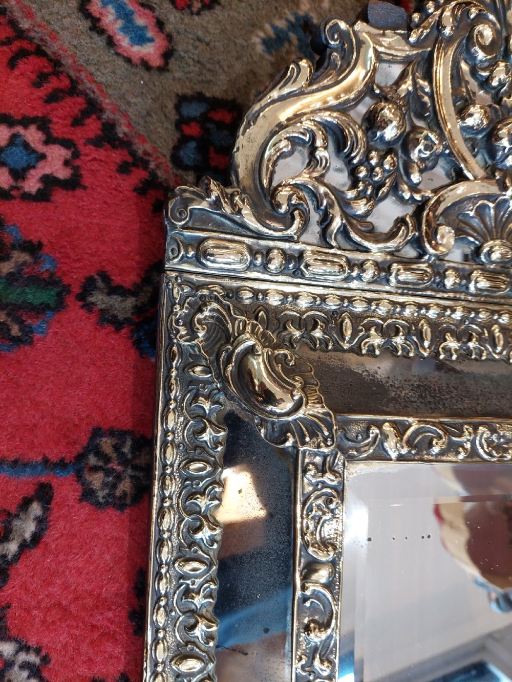 An early nineteenth-century Dutch style wall mirror featuring embossed repousse brass metalwork and a decorated crest over a central glass plate. View V