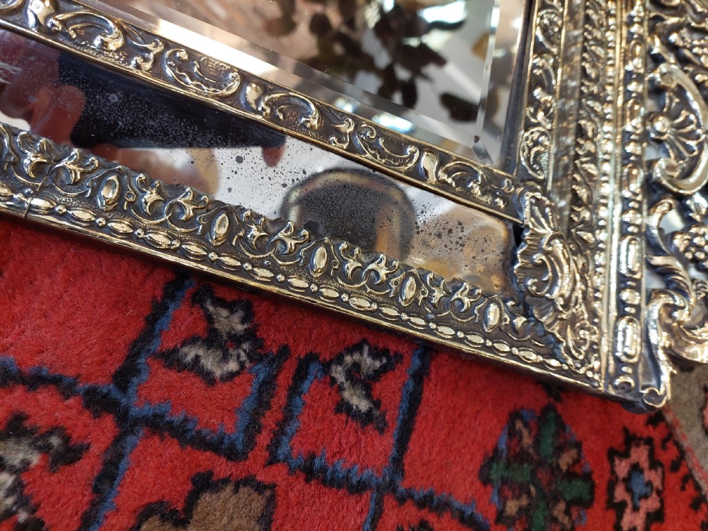 An early nineteenth-century Dutch style wall mirror featuring embossed repousse brass metalwork and a decorated crest over a central glass plate. View VI