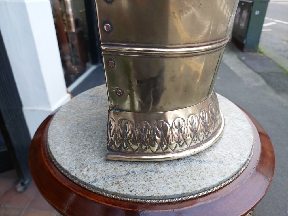 A polished Edwardian brass half-moon stick stand featuring embossed decorative borders and a dark wooden carrying handle. View IV