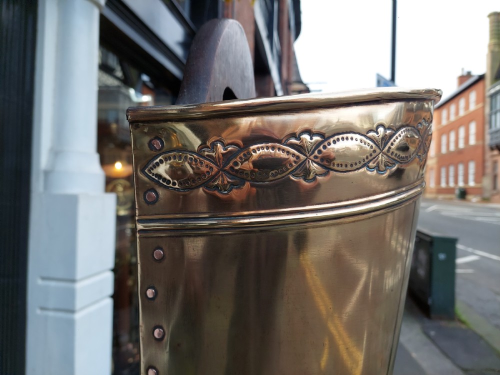 A polished Edwardian brass half-moon stick stand featuring embossed decorative borders and a dark wooden carrying handle. View V