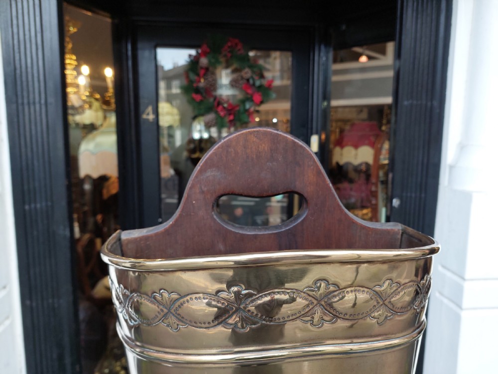 A polished Edwardian brass half-moon stick stand featuring embossed decorative borders and a dark wooden carrying handle. View VII