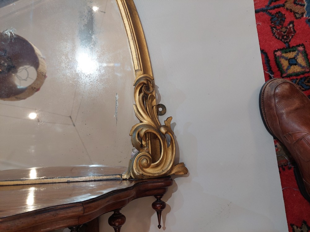 An arched Victorian giltwood pier mirror featuring ornate acanthus leaf cresting mounted over a dark carved wooden bracket shelf. View III