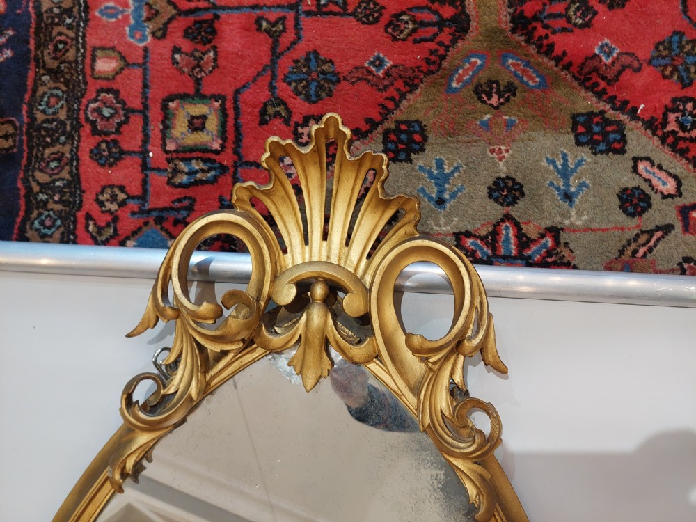 An arched Victorian giltwood pier mirror featuring ornate acanthus leaf cresting mounted over a dark carved wooden bracket shelf. View IV