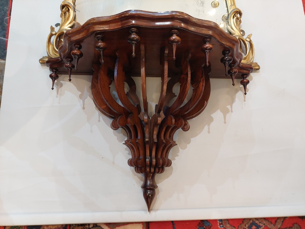 An arched Victorian giltwood pier mirror featuring ornate acanthus leaf cresting mounted over a dark carved wooden bracket shelf. View V