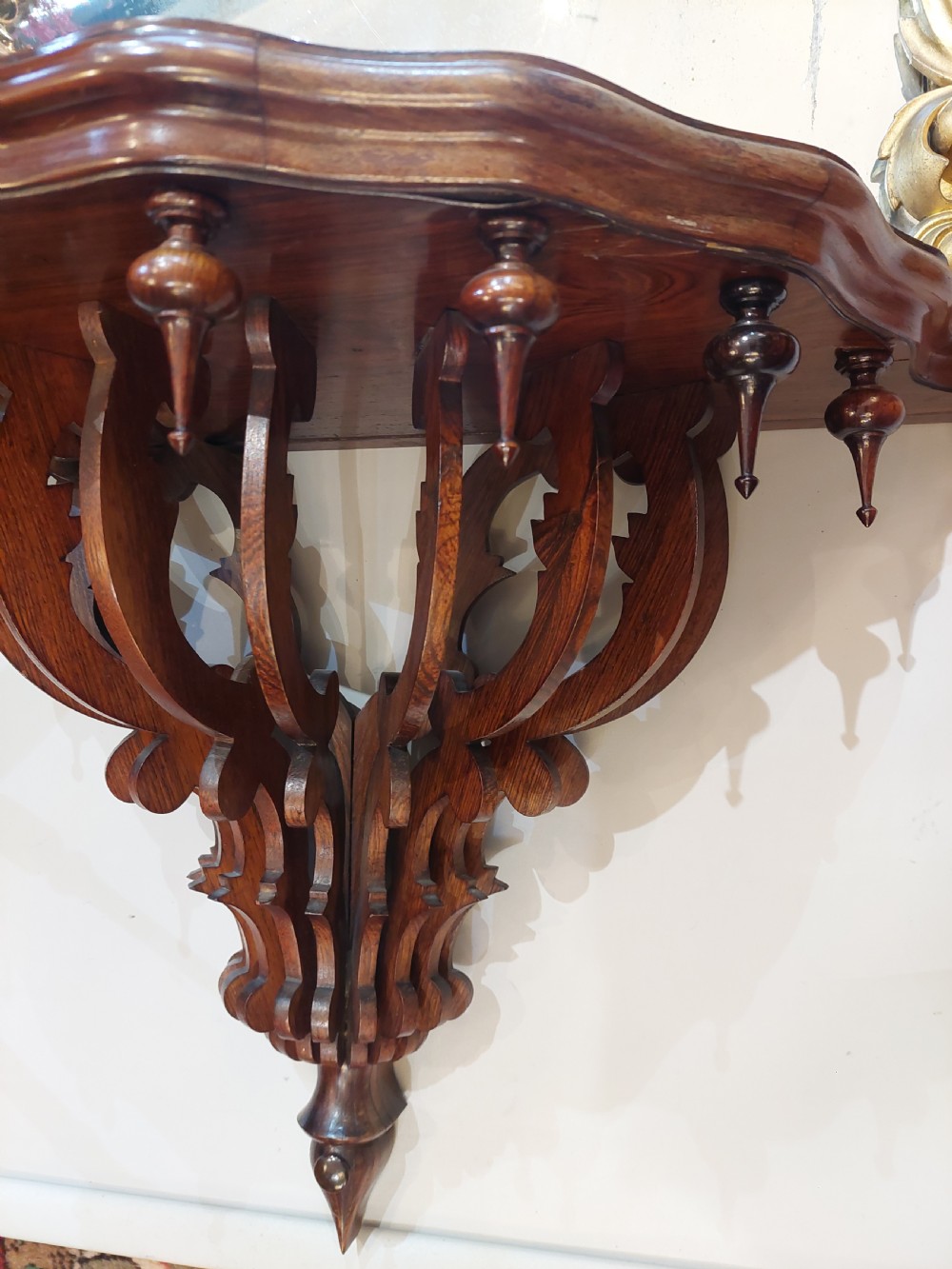 An arched Victorian giltwood pier mirror featuring ornate acanthus leaf cresting mounted over a dark carved wooden bracket shelf. View VI