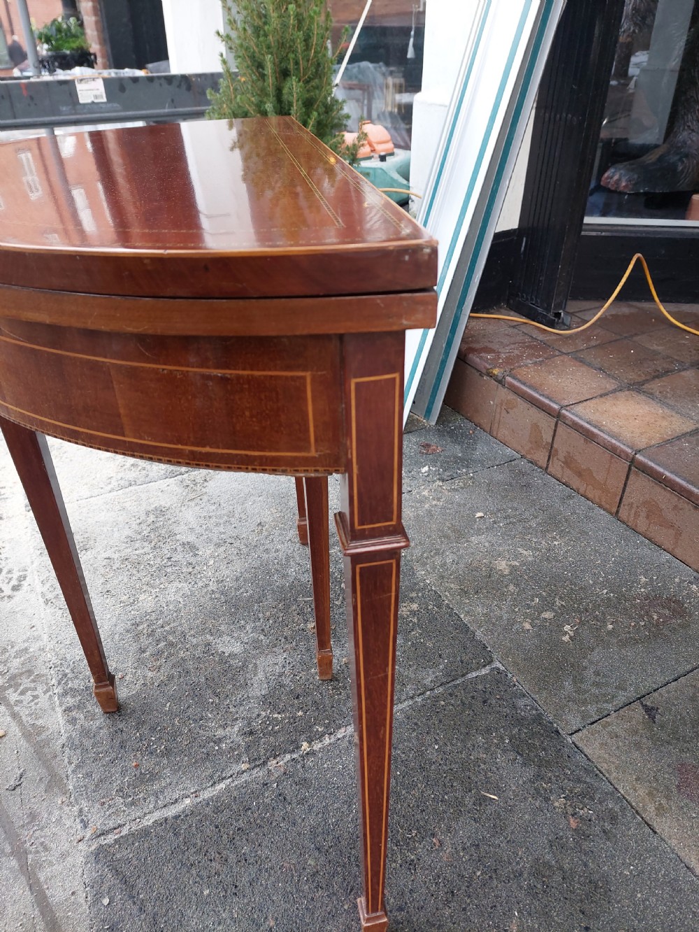 An Edwardian demilune card table crafted from mahogany with fine boxwood stringing and square tapered legs. View II