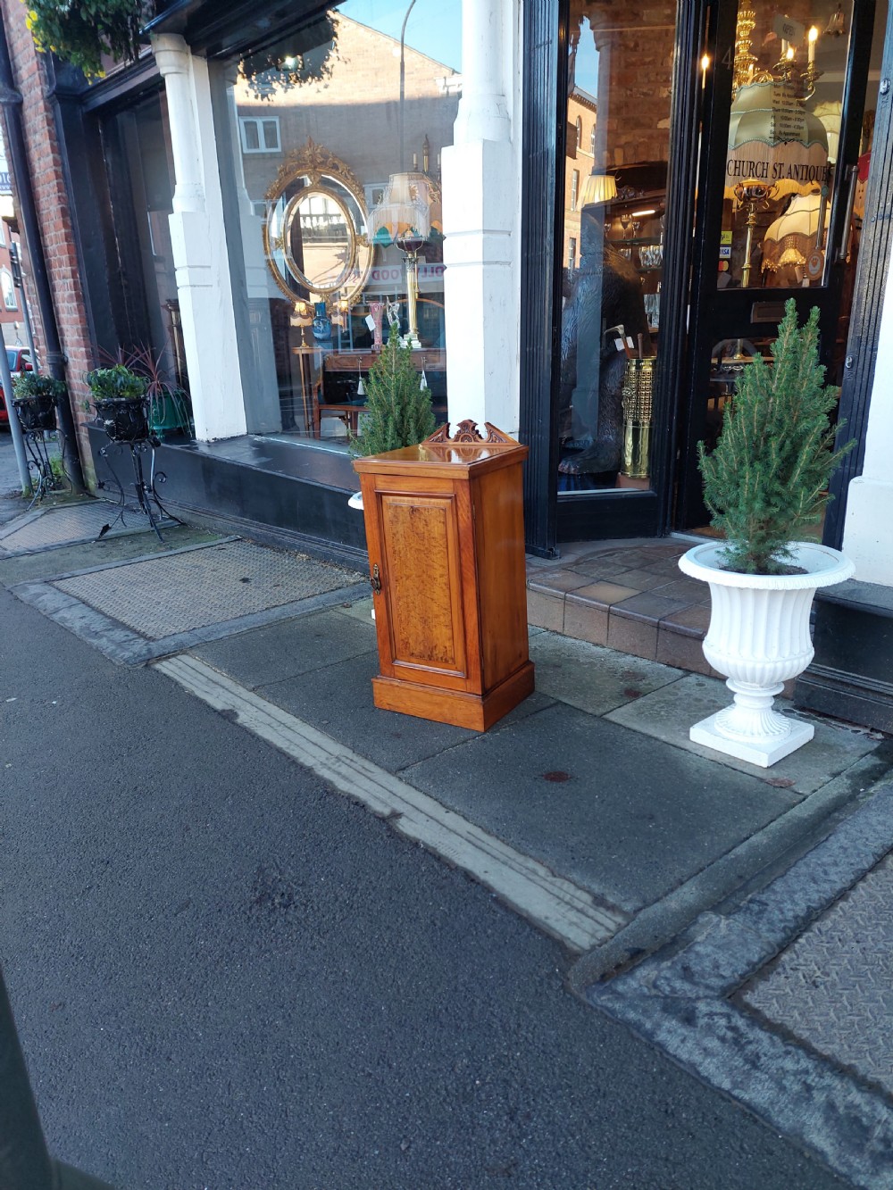 An Edwardian walnut bedside cabinet featuring a single cupboard door with a figured wood panel, a carved top gallery, and a solid plinth base. View II