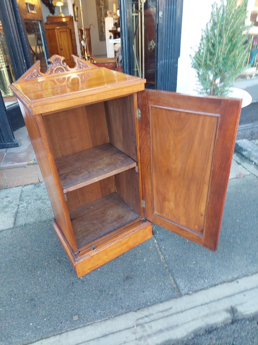 An Edwardian walnut bedside cabinet featuring a single cupboard door with a figured wood panel, a carved top gallery, and a solid plinth base. View V