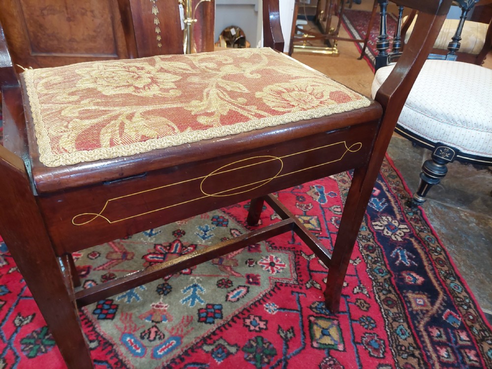 An Edwardian mahogany piano stool featuring swept armrests, an inlaid back splat, a patterned fabric seat, and geometric line inlay. View III