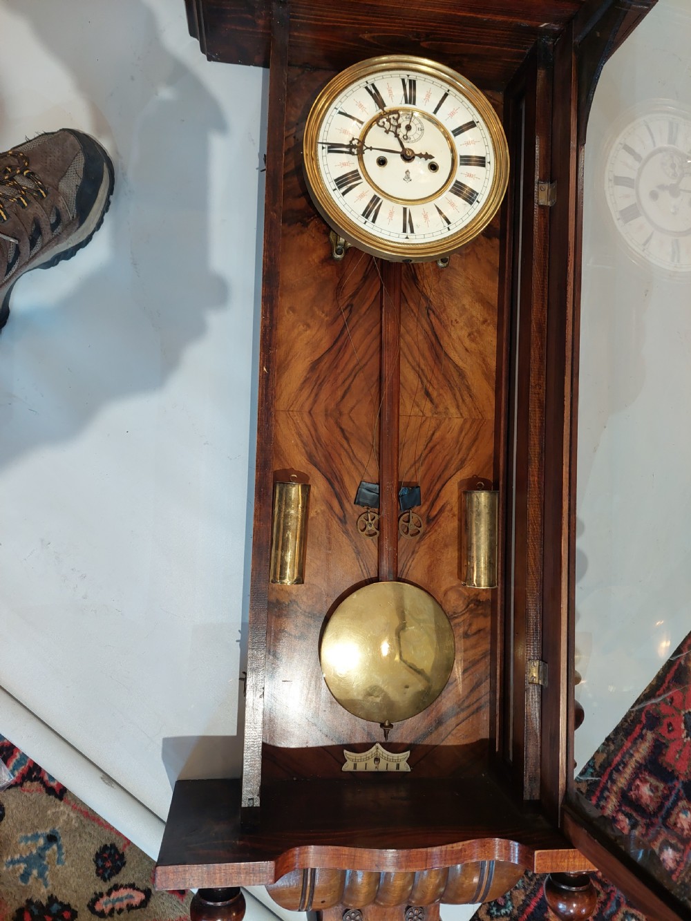 Late Victorian double weight Vienna wall clock featuring a carved walnut case topped with an eagle pediment, turned side finials, a glazed door revealing twin brass weights, and a white dial with Roman numerals. View VI