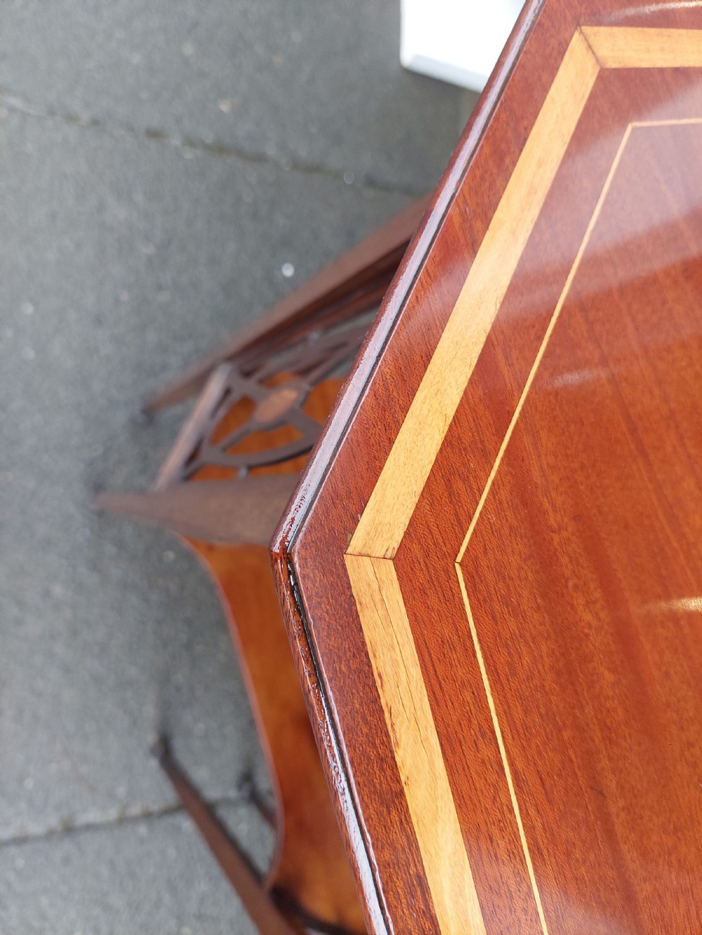 An Edwardian octagonal mahogany occasional table featuring inlaid satinwood borders, pierced side fretwork panels, and a lower tier supported by tapered square legs. View VII