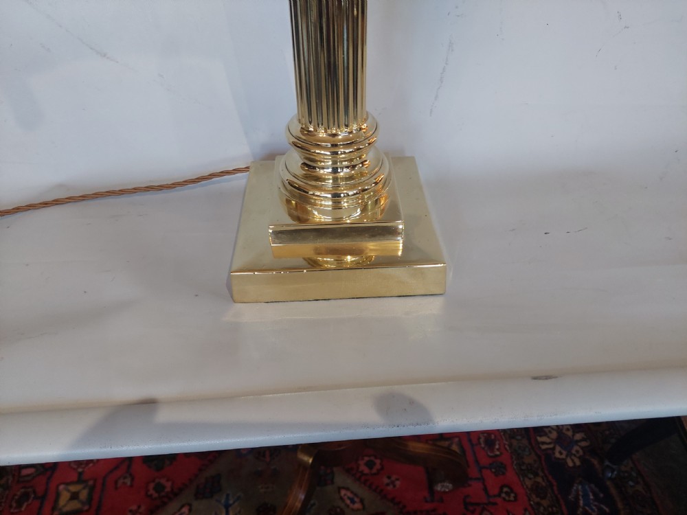 An Edwardian brass table lamp with a fluted Corinthian column base, topped with a cream patterned fabric shade with long fringe trim. View III
