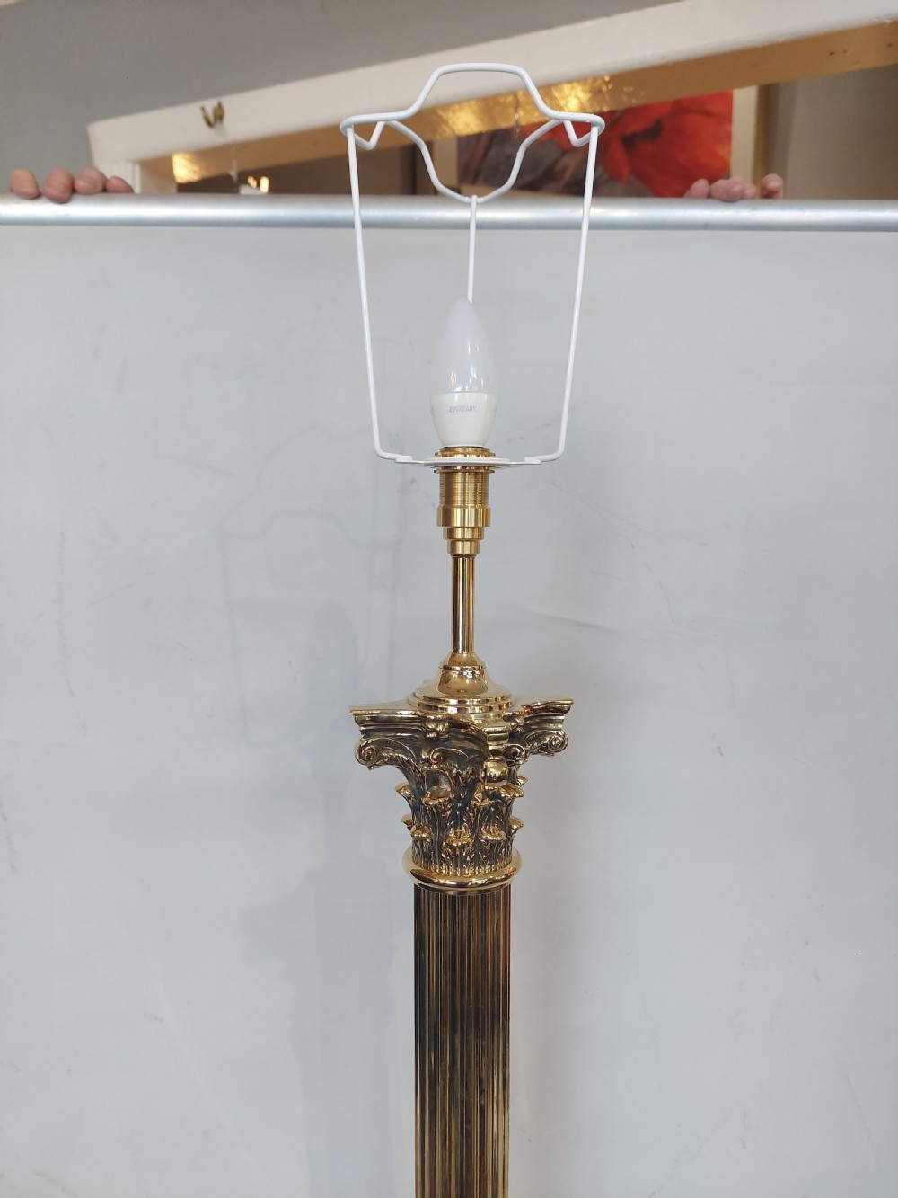 An Edwardian brass table lamp with a fluted Corinthian column base, topped with a cream patterned fabric shade with long fringe trim. View VII