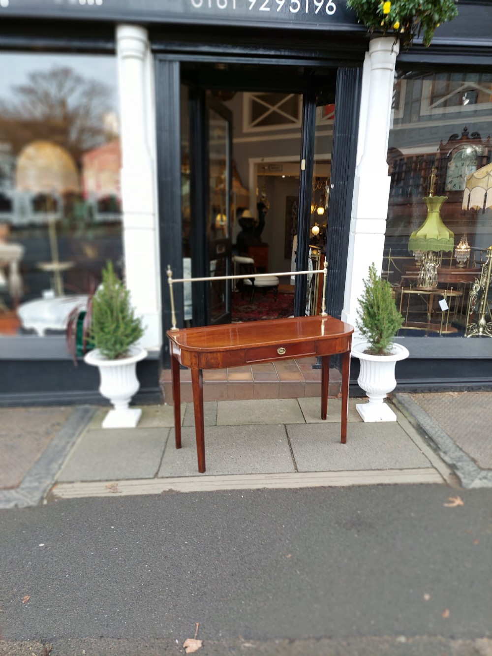 A Georgian mahogany hall table with a rounded bowfront top, a single central drawer with brass handle, a brass finial gallery rail, and four square tapered legs. View II