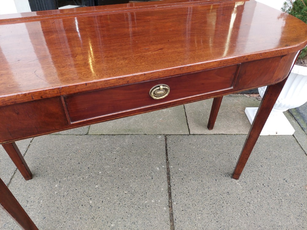 A Georgian mahogany hall table with a rounded bowfront top, a single central drawer with brass handle, a brass finial gallery rail, and four square tapered legs. View III