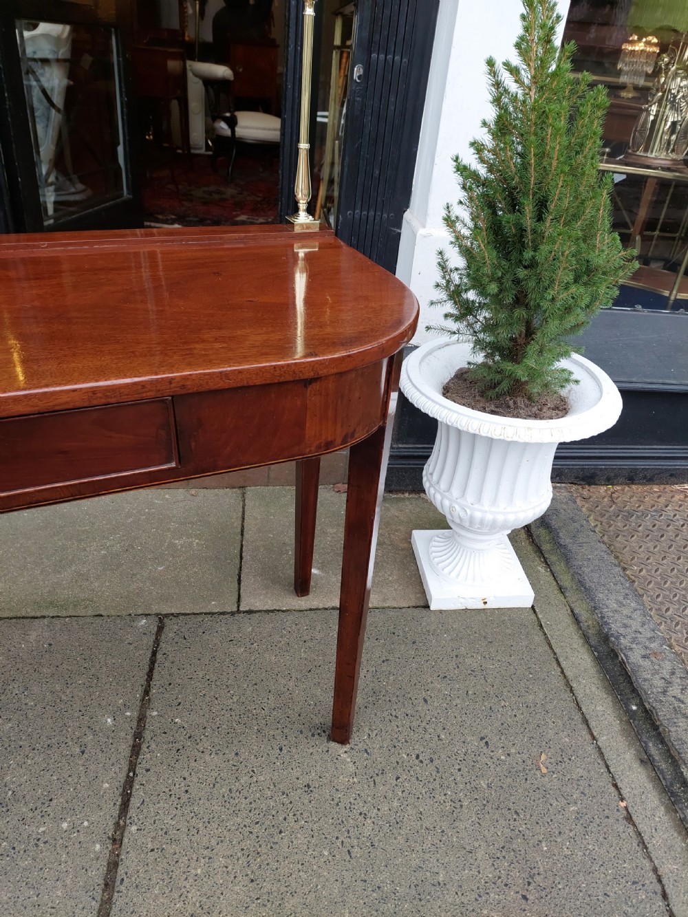 A Georgian mahogany hall table with a rounded bowfront top, a single central drawer with brass handle, a brass finial gallery rail, and four square tapered legs. View IV