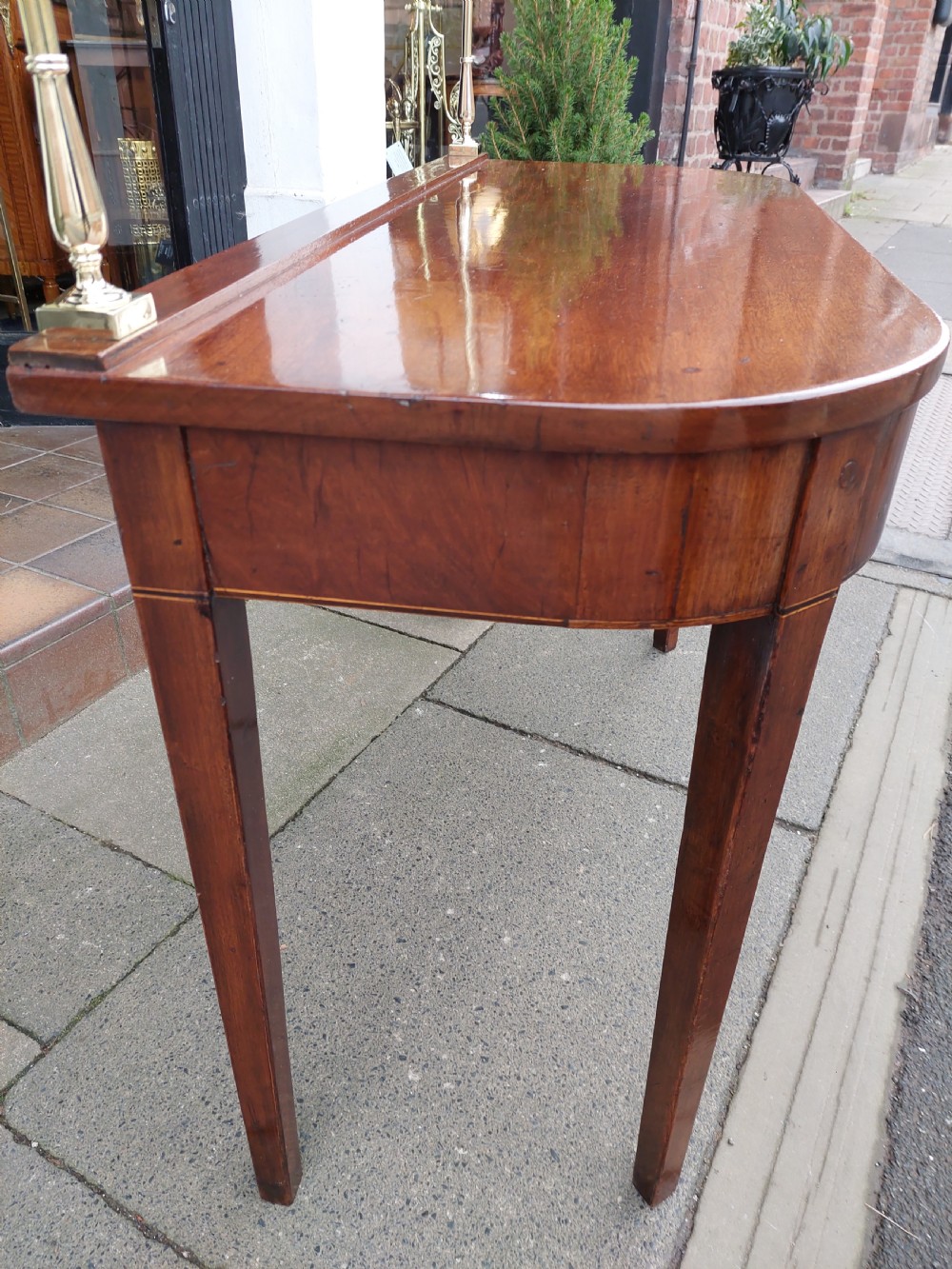 A Georgian mahogany hall table with a rounded bowfront top, a single central drawer with brass handle, a brass finial gallery rail, and four square tapered legs. View IX