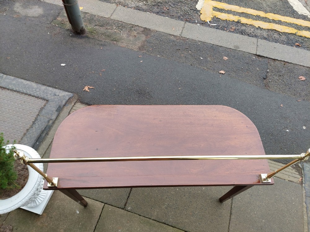 A Georgian mahogany hall table with a rounded bowfront top, a single central drawer with brass handle, a brass finial gallery rail, and four square tapered legs. View X