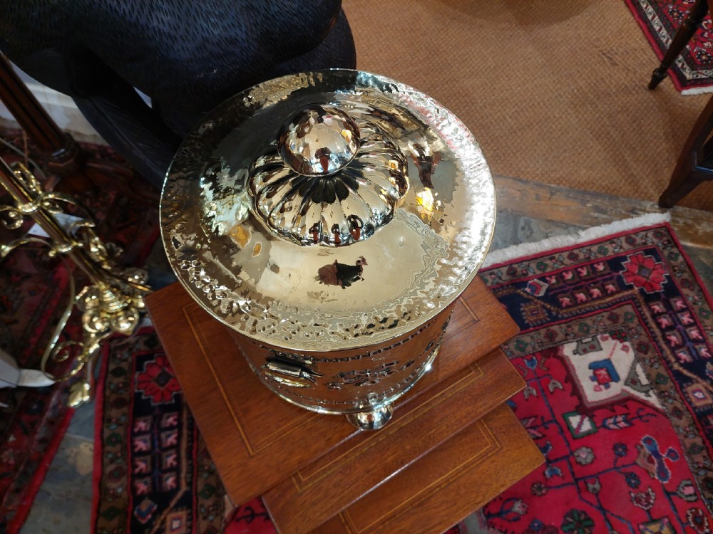 A cylindrical Victorian brass coal receiver featuring embossed garland motifs, beaded horizontal bands, side ring handles, and a fitted domed lid with a finial. View V