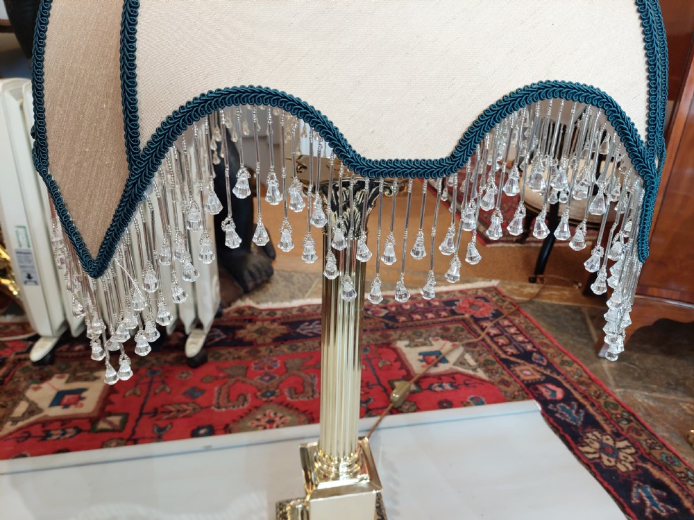 A brass column table lamp featuring a reeded stem, stepped square base, and a cream fabric dome shade trimmed with dark braid and clear glass droplet fringe. View V