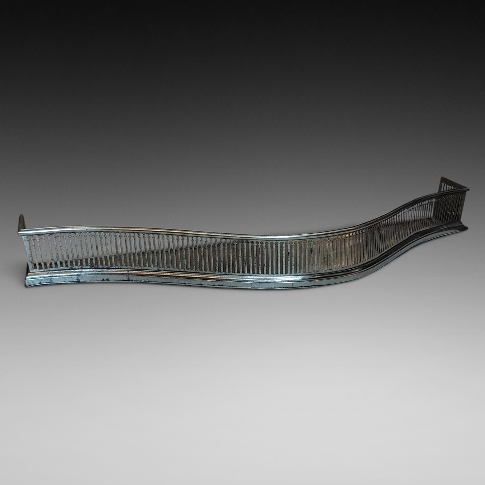 A polished steel Georgian fireplace fender featuring a serpentine front profile and vertical pierced slat fretwork.