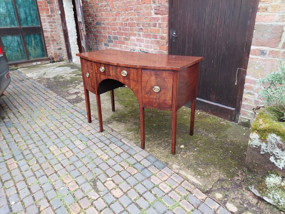 A late 18th-century mahogany bowfront sideboard featuring an arched central apron, oval-patterned veneered drawer fronts, brass drop handles, and six square tapered legs. View II