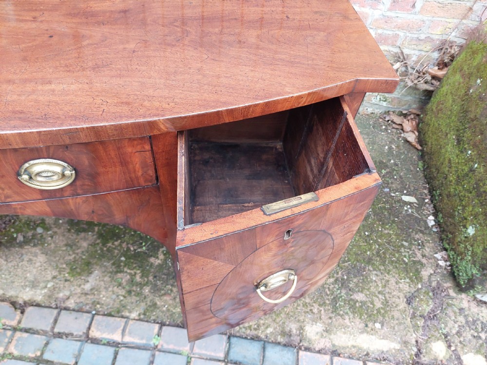 A late 18th-century mahogany bowfront sideboard featuring an arched central apron, oval-patterned veneered drawer fronts, brass drop handles, and six square tapered legs. View VIII