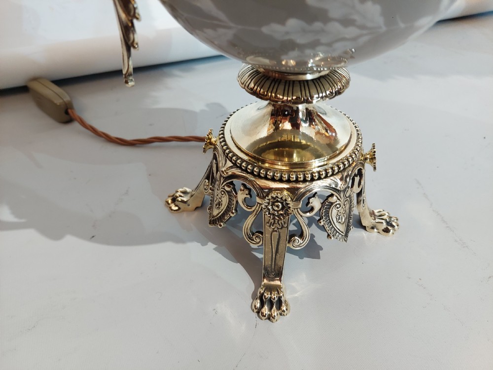 A pair of late 19th-century gilt brass and grey porcelain table lamps featuring fringed fabric lampshades. View X