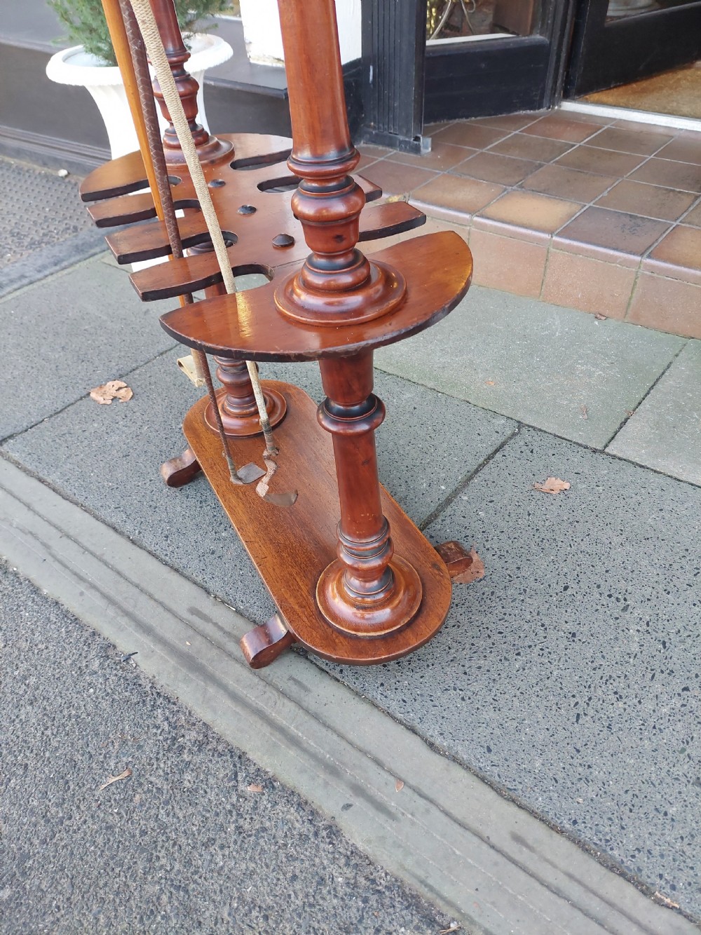 A Victorian turned mahogany whip stand featuring finial uprights, multiple upper pegs, a notched central shelf, and a solid base on feet. View V