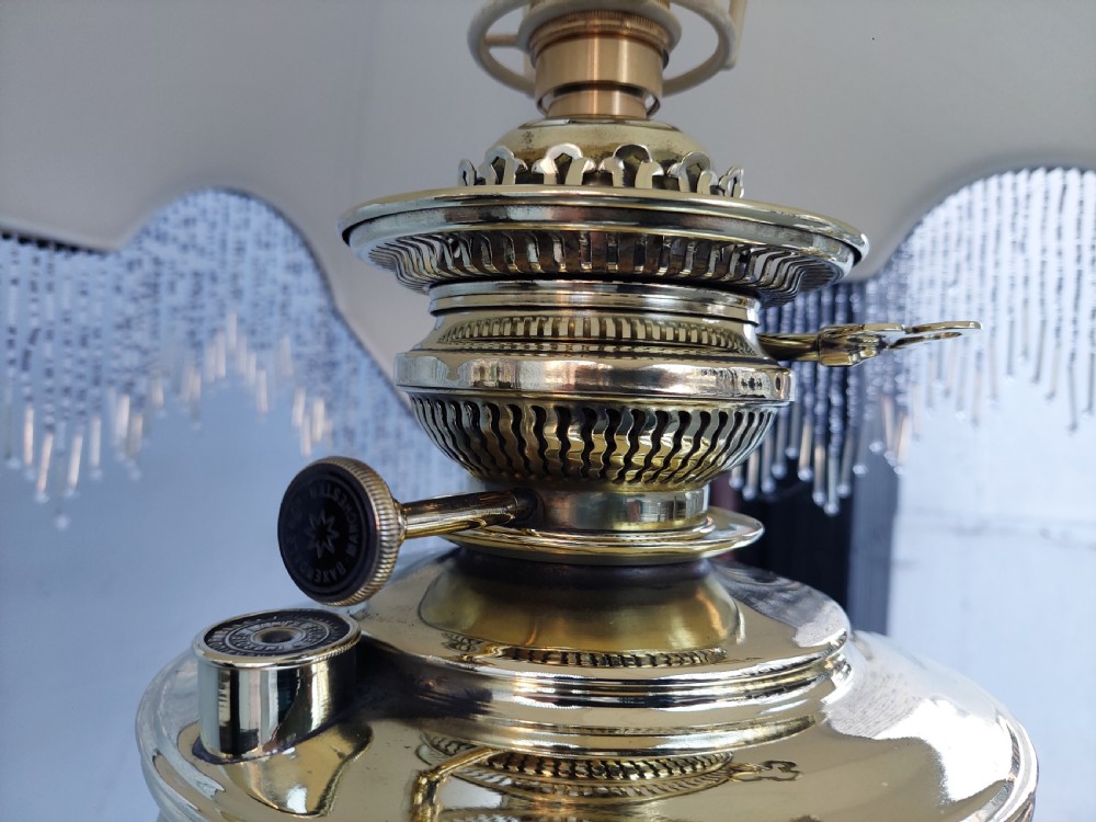 A late nineteenth-century Corinthian column oil lamp featuring a fluted stem, polished metal reservoir, and a white fabric dome shade trimmed with blue piping and long glass bead fringe. View VII
