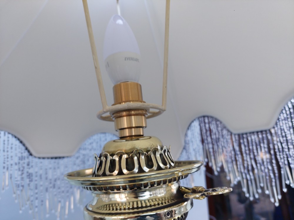 A late nineteenth-century Corinthian column oil lamp featuring a fluted stem, polished metal reservoir, and a white fabric dome shade trimmed with blue piping and long glass bead fringe. View VIII