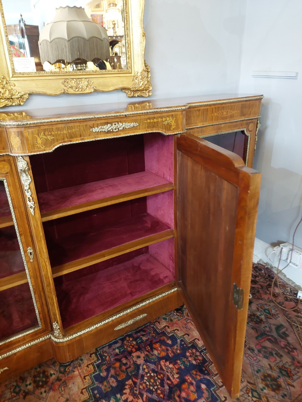 A nineteenth-century Victorian breakfront cabinet in burr walnut with marquetry inlay, gilt metal mounts, a central panelled door, and two side glazed display sections with velvet lining. View VI