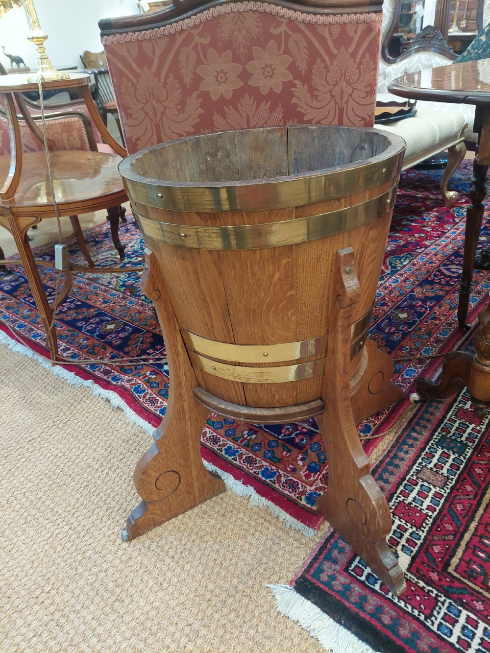 An Arts and Crafts oak planter featuring coopered wood staves secured with broad brass bands, supported on three carved scrolled timber legs. View V