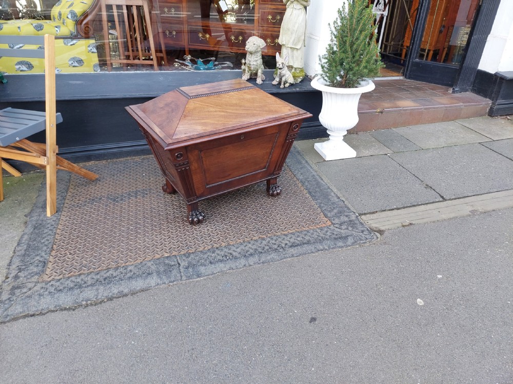 A late Regency flame mahogany sarcophagus cellarette featuring a faceted hinged lid, carved lion paw feet, and beaded edge moulding. View VI