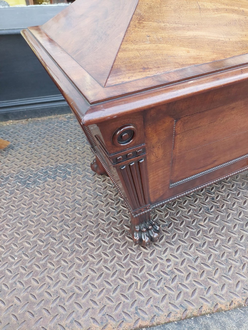 A late Regency flame mahogany sarcophagus cellarette featuring a faceted hinged lid, carved lion paw feet, and beaded edge moulding. View VIII