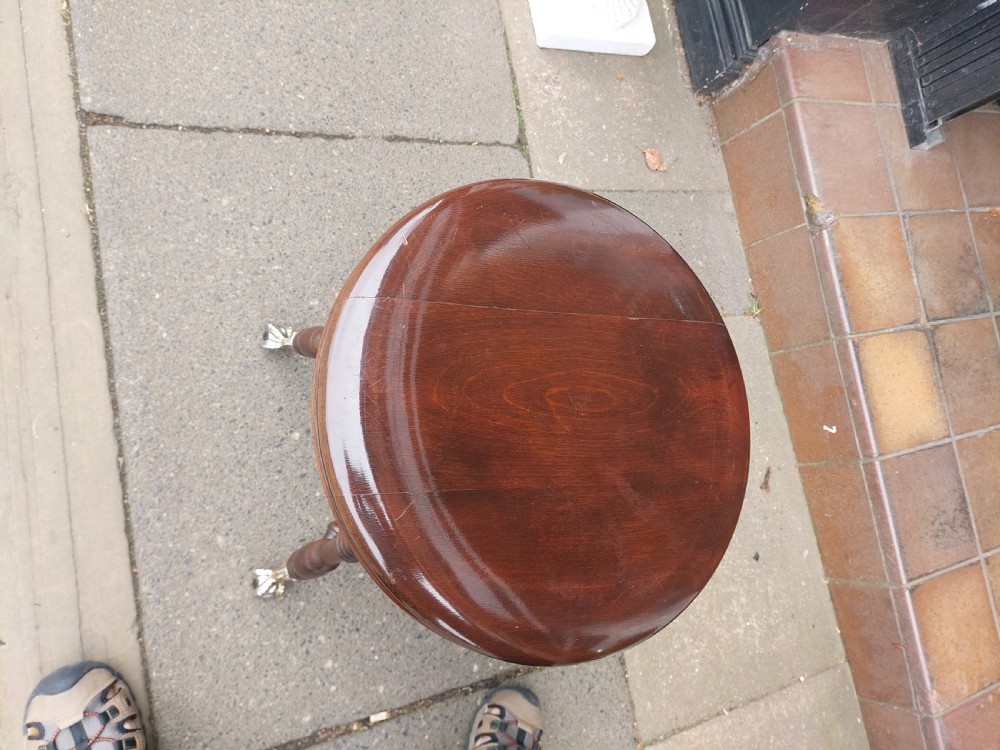 An early 20th-century dark mahogany piano stool featuring a circular swivel top, turned spindled legs, central pillar, and metal claw feet with glass balls. View VI