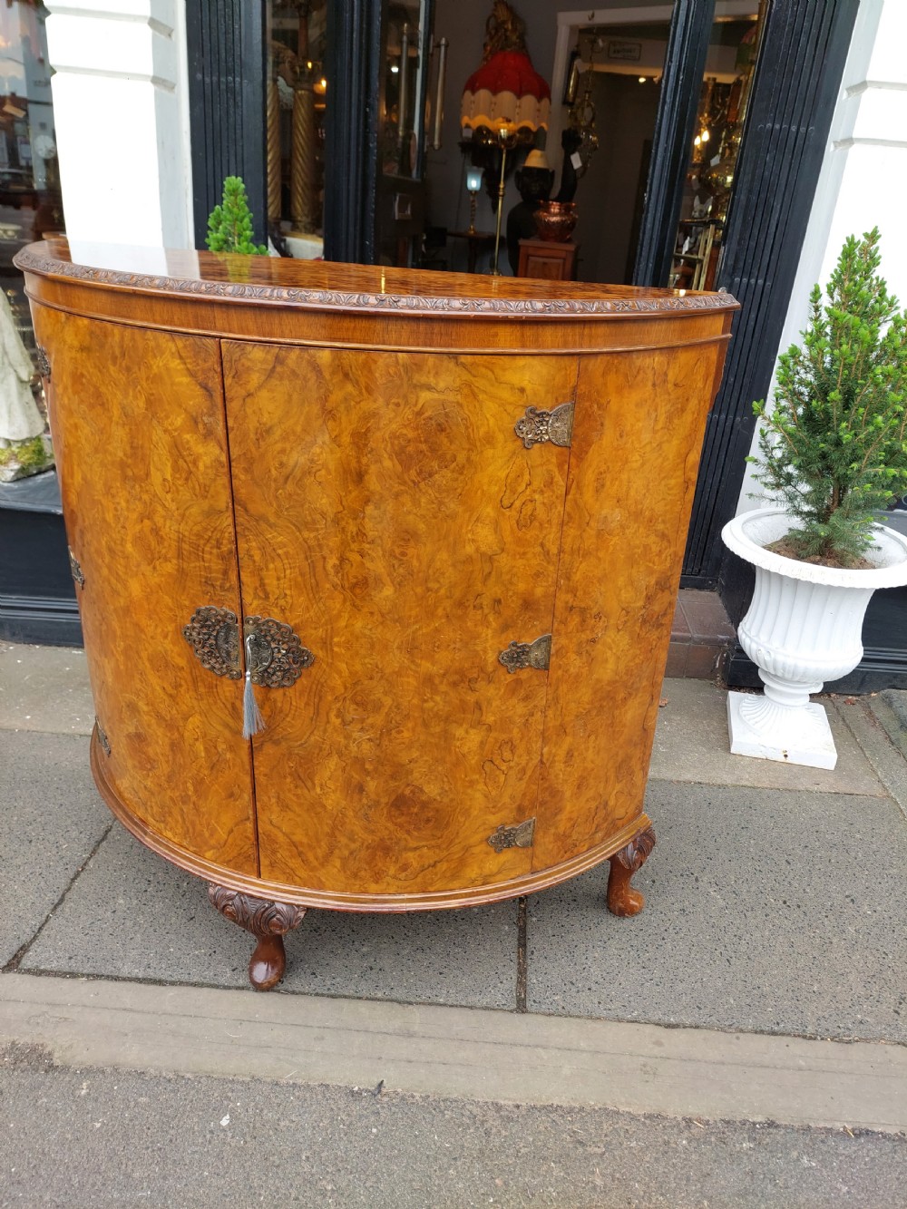 An early twentieth-century demi-lune drinks cabinet crafted from golden burr walnut veneer with carved cabriole legs and brass hardware. View IV