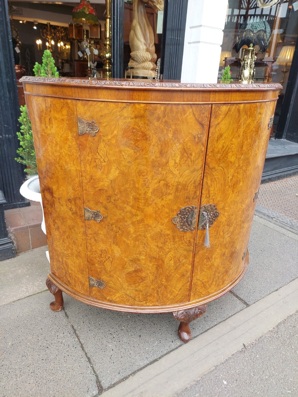 An early twentieth-century demi-lune drinks cabinet crafted from golden burr walnut veneer with carved cabriole legs and brass hardware. View V