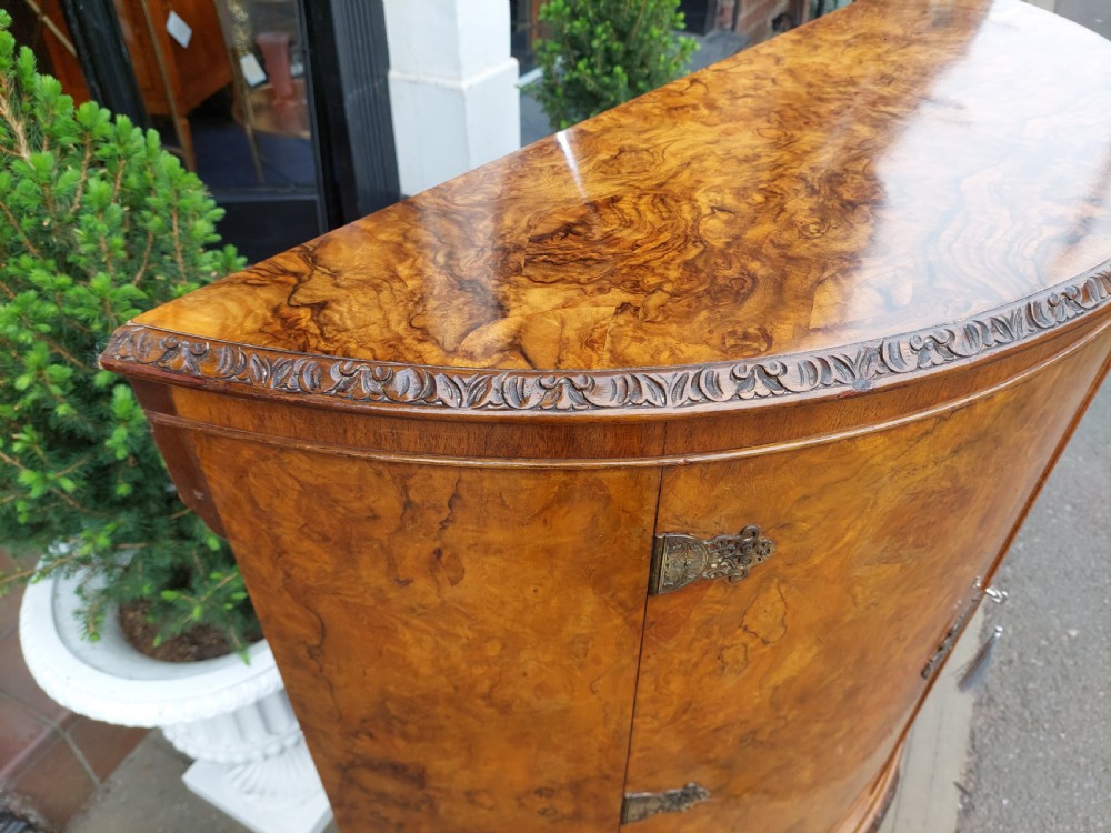 An early twentieth-century demi-lune drinks cabinet crafted from golden burr walnut veneer with carved cabriole legs and brass hardware. View VI