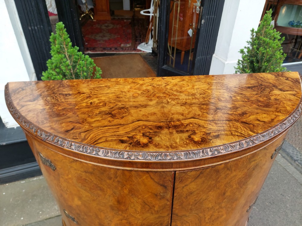 An early twentieth-century demi-lune drinks cabinet crafted from golden burr walnut veneer with carved cabriole legs and brass hardware. View VII