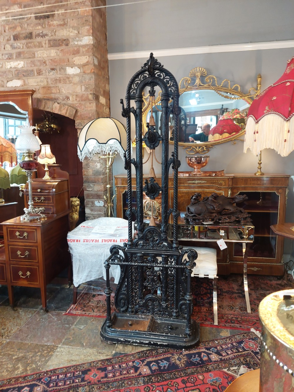 An ornate 19th-century black cast iron hall stand featuring coat hooks, intricate scrollwork, umbrella compartments, and a removable drip tray base. View II