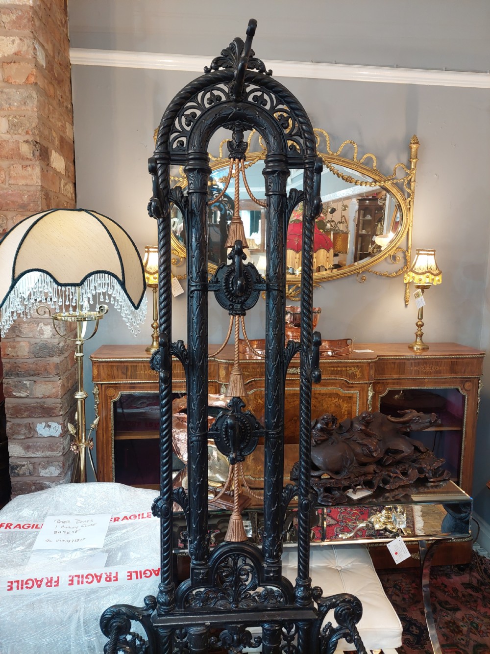 An ornate 19th-century black cast iron hall stand featuring coat hooks, intricate scrollwork, umbrella compartments, and a removable drip tray base. View III