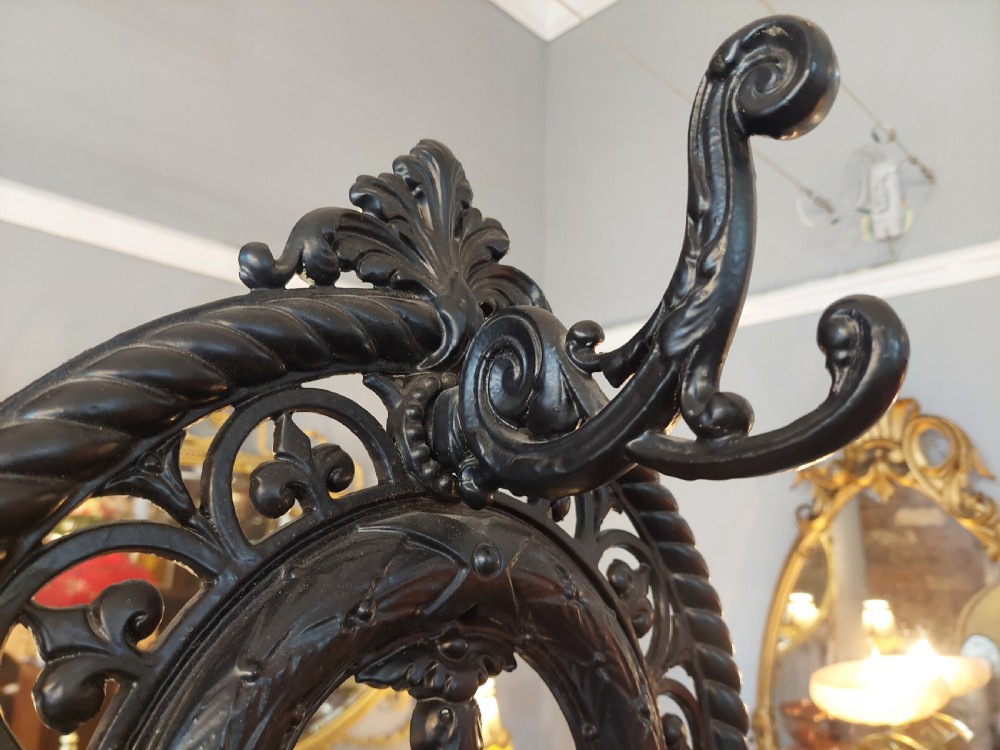 An ornate 19th-century black cast iron hall stand featuring coat hooks, intricate scrollwork, umbrella compartments, and a removable drip tray base. View V