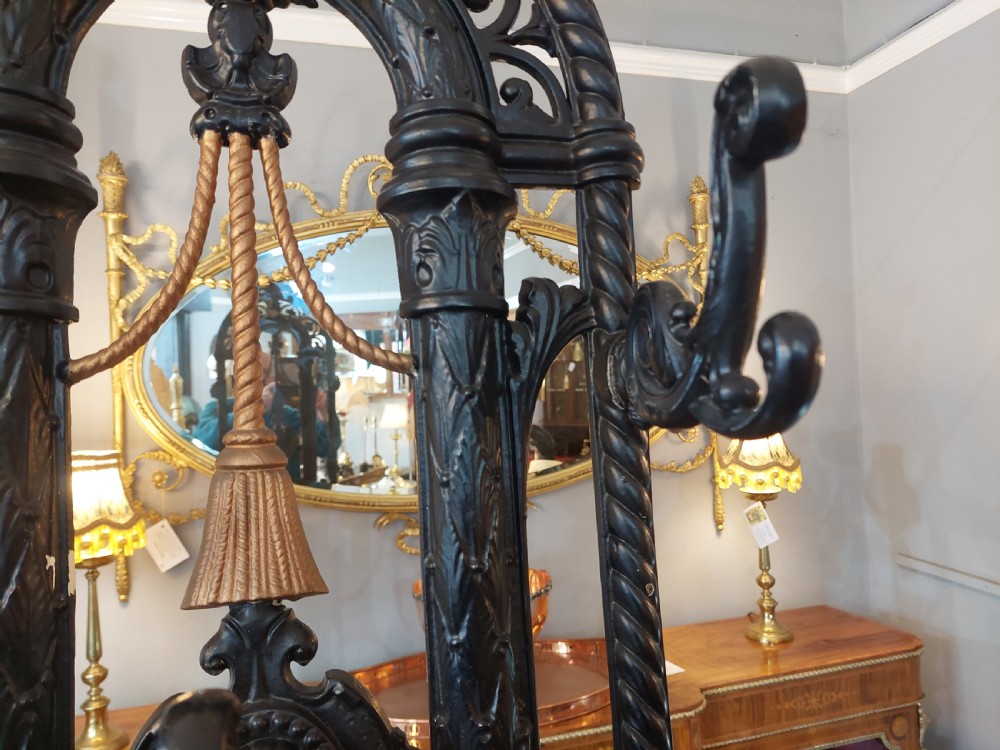 An ornate 19th-century black cast iron hall stand featuring coat hooks, intricate scrollwork, umbrella compartments, and a removable drip tray base. View VI