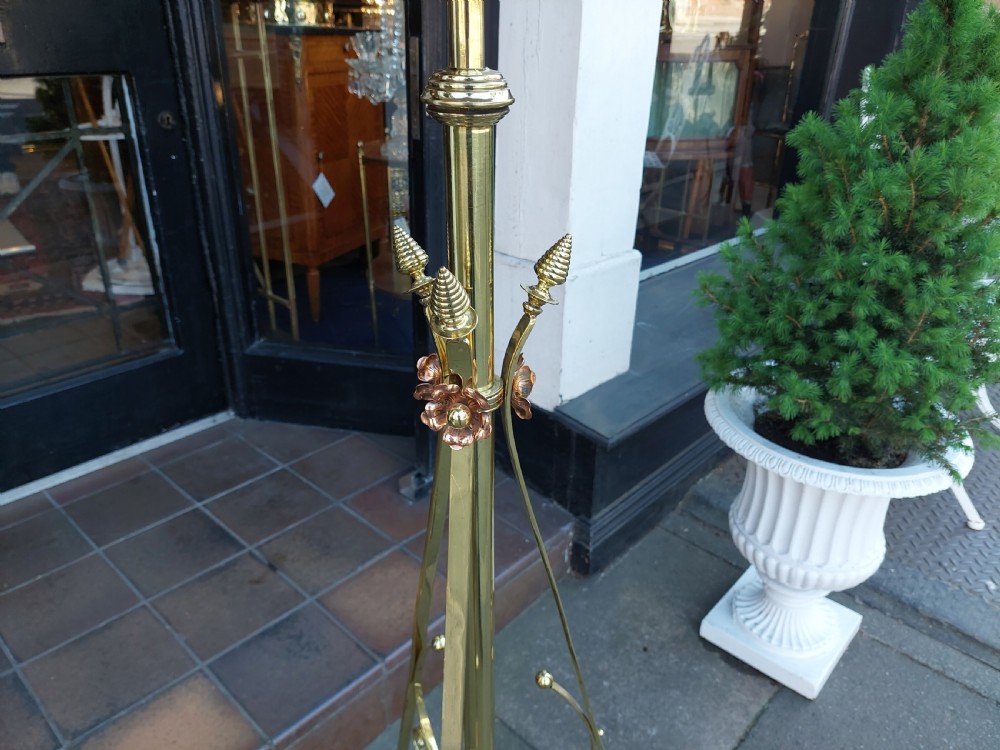 An Arts and Crafts brass standard floor lamp featuring a scrollwork tripod base, floral copper accents, and a fringe-trimmed domed shade. View II